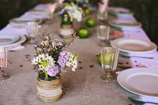 A softly lived-in country-style table with linen cloth, simple dishes, glass cups, and rustic floral jars. Warm, real, and inviting